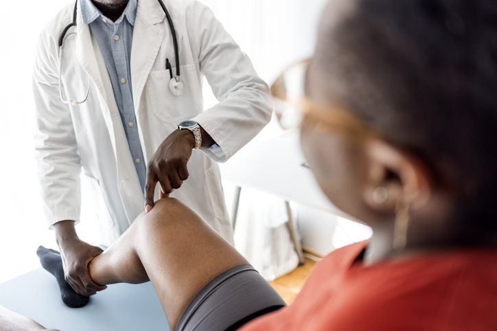 Unrecognizable male physiotherapist examining leg injury on a woman lying down.